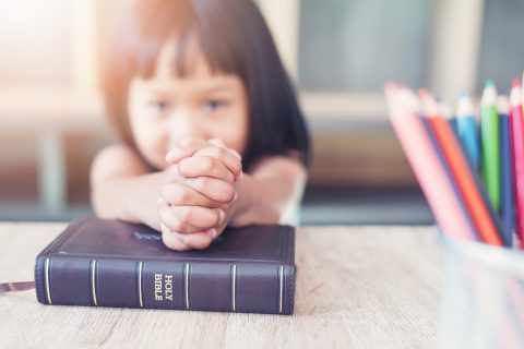 Little Asian girl pray with bible in classroom at school, bible study concept