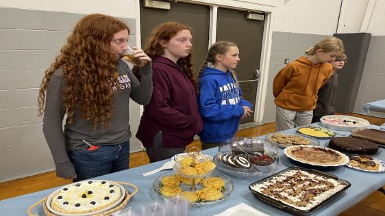 AJA students stand next to the dessert bake-off table. 